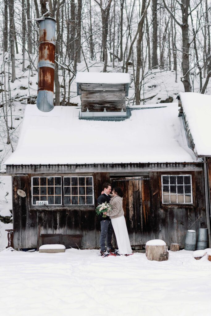 bride and groom embrace outside of sugar shack in vermont winter elopement