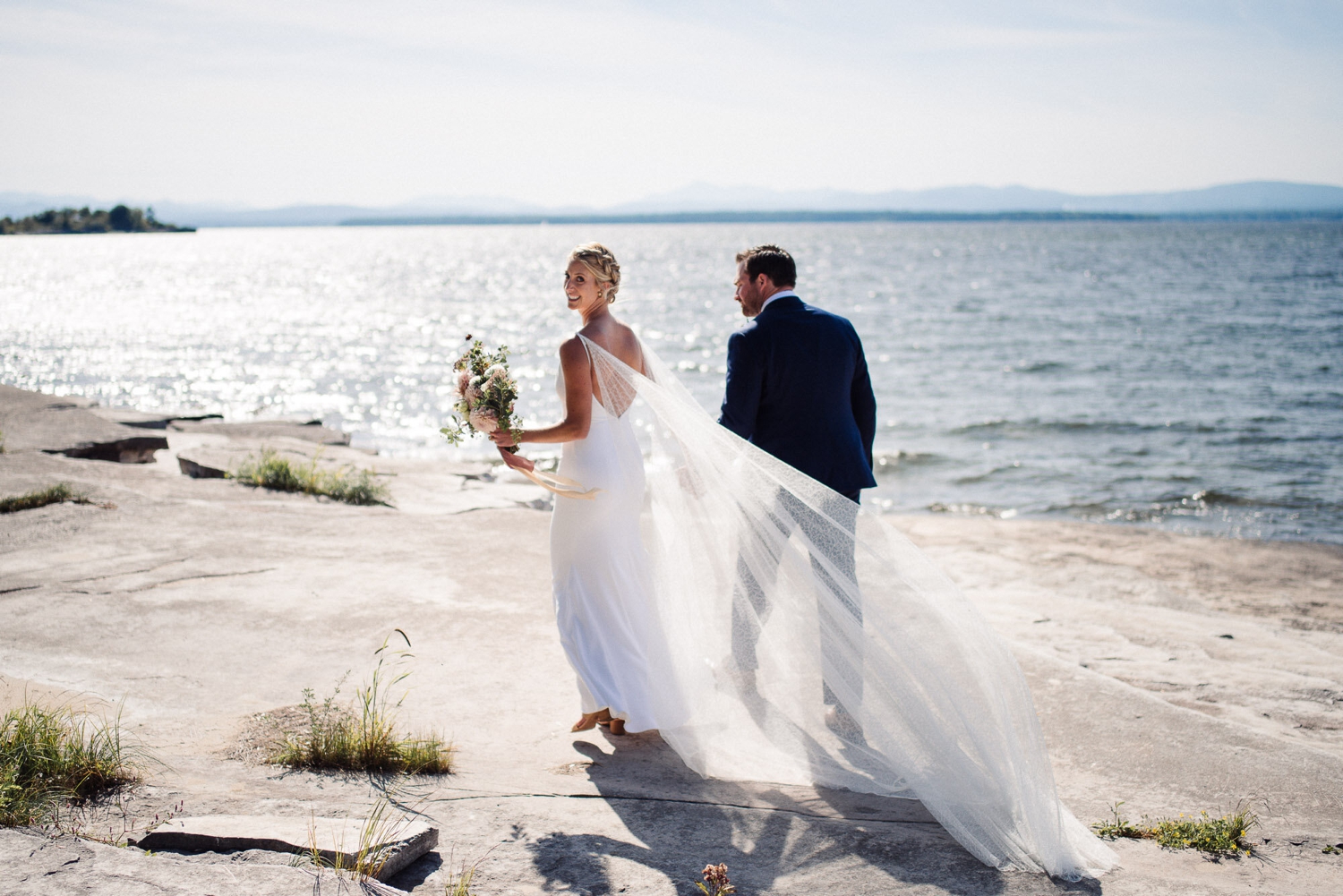 Bride and groom holding hands on the shore of Lake Champlain