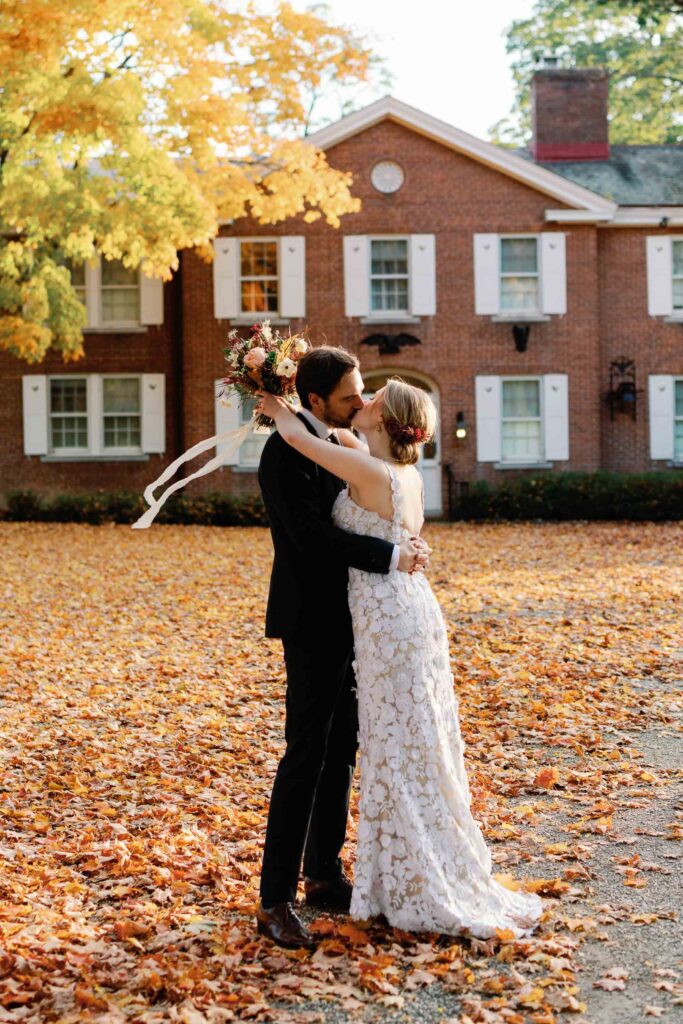 bride and groom kiss at brick house shelburne museum with fall leaves all around and golden sunlight