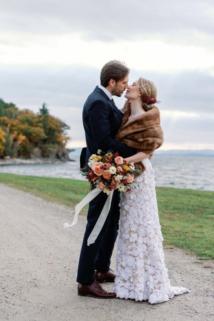 bride and groom kiss next to lake champlain wedding in shelburne vt with fall florals in the wind