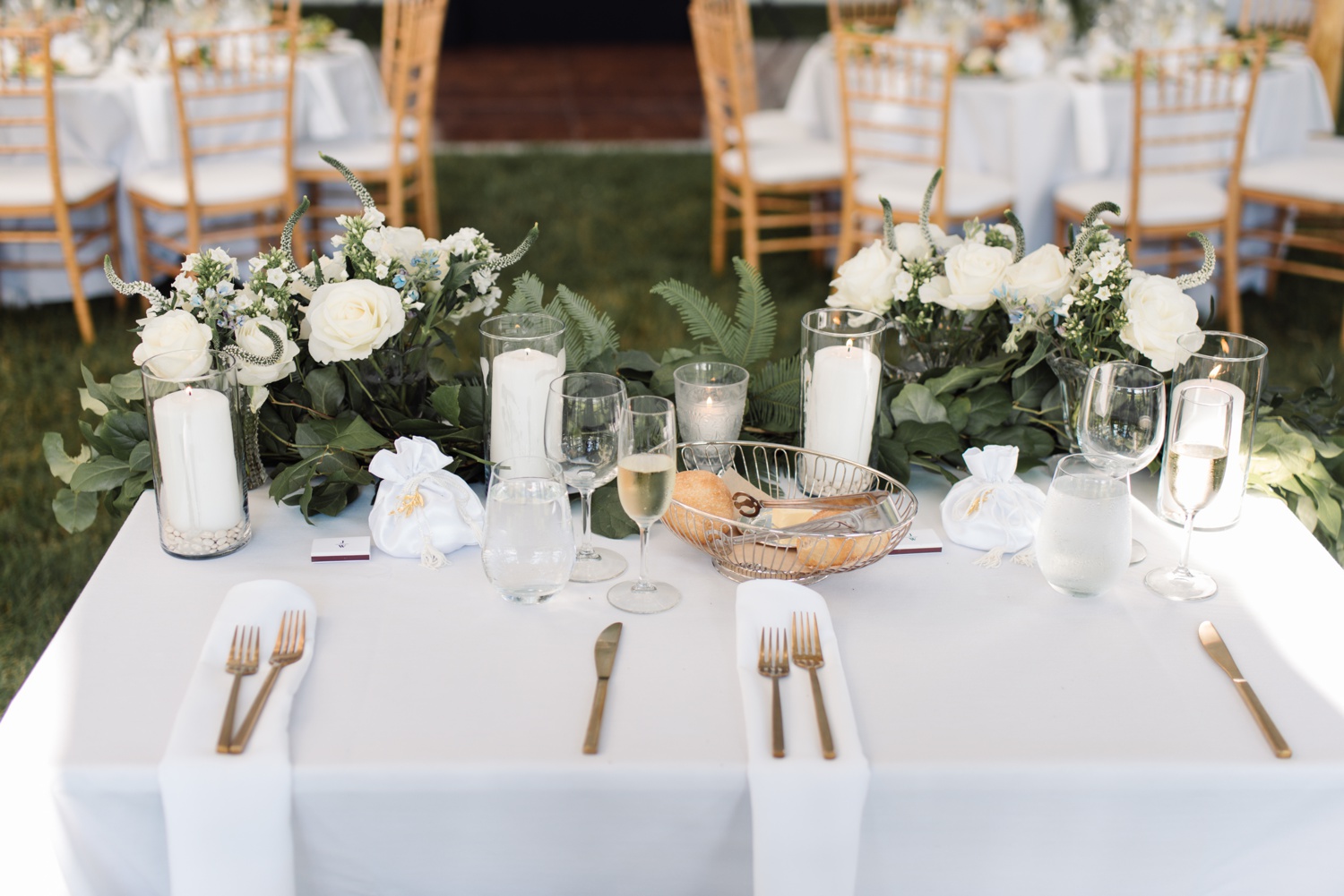 White table linens, gold cutlery, blue and white florals, and white taper candles for a summer tented wedding reception