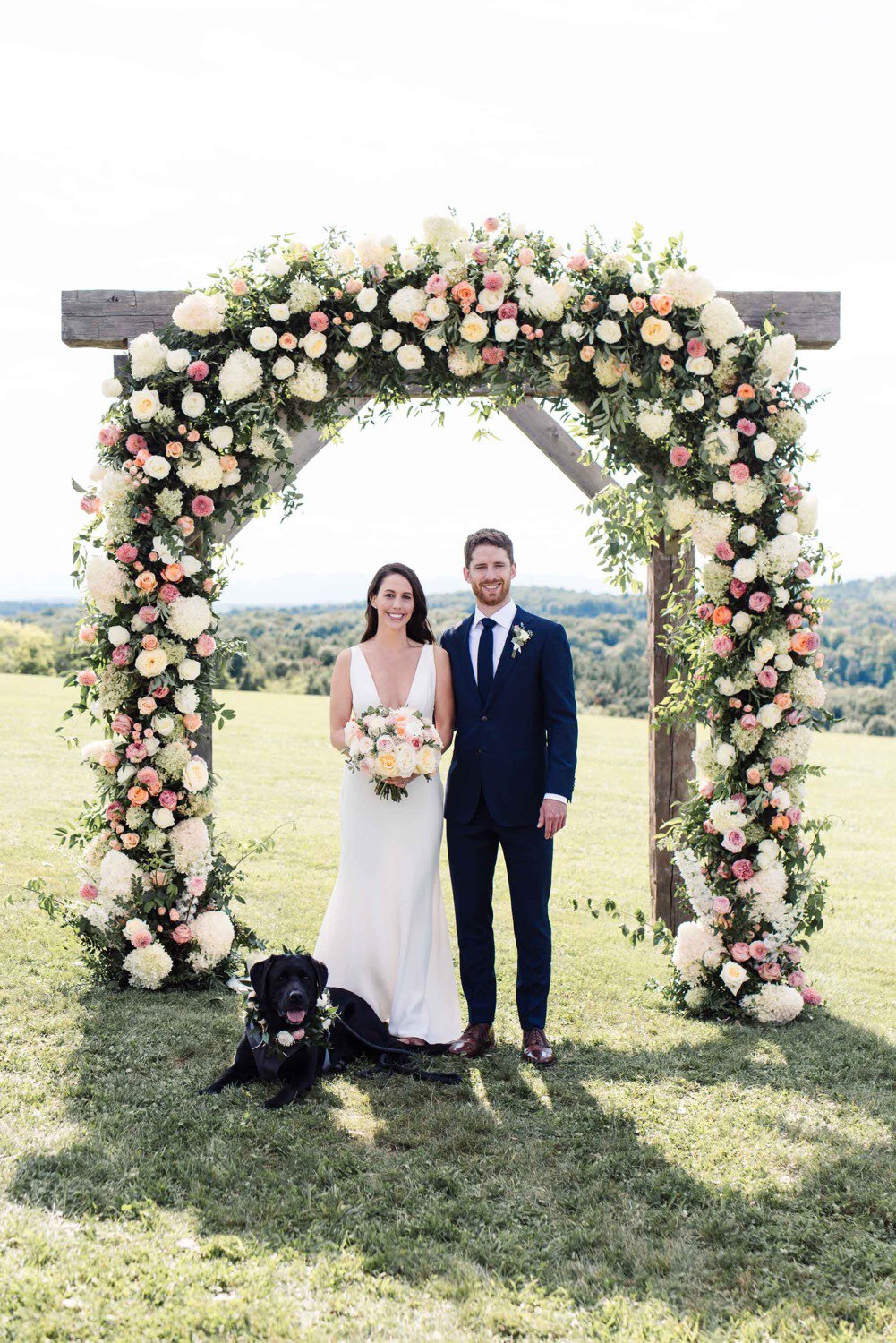 Bride and groom with their dog underneath lush outdoor arbor by Clayton Floral