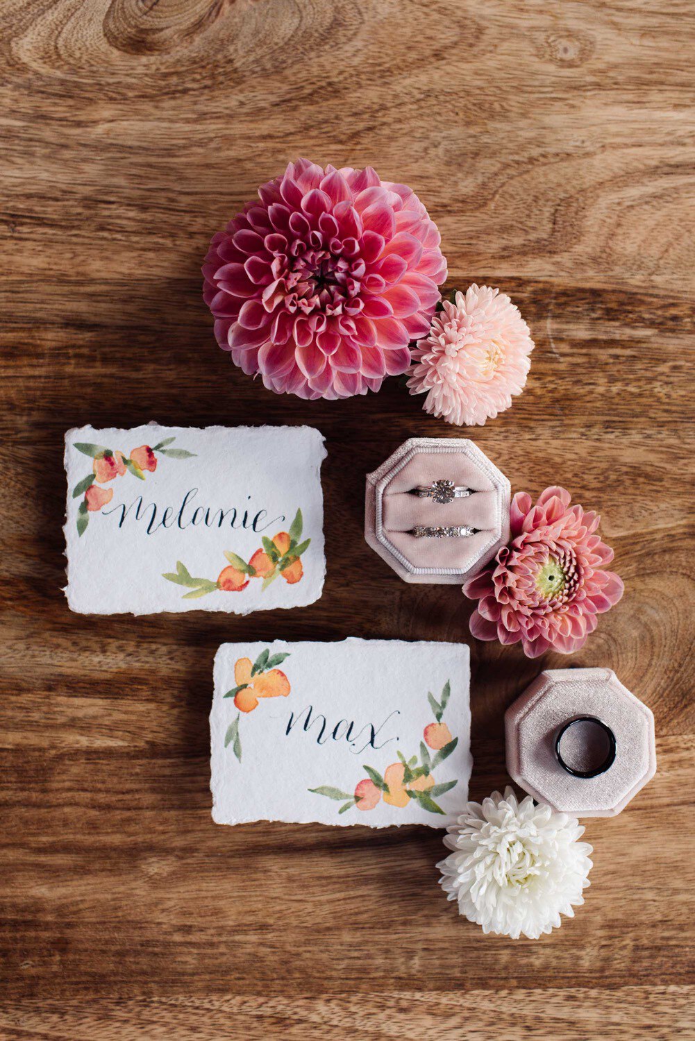 Wedding rings, flowers, and hand painted place cards on wood background