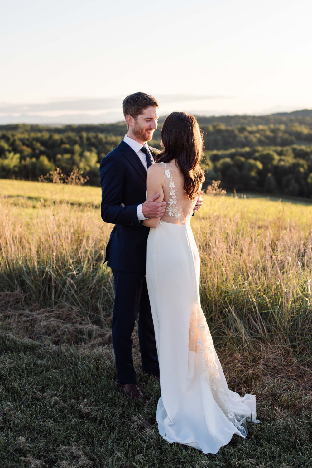 Bride and groom embrace at sunset overlooking Adirondacks in Alexandra Grecco gown