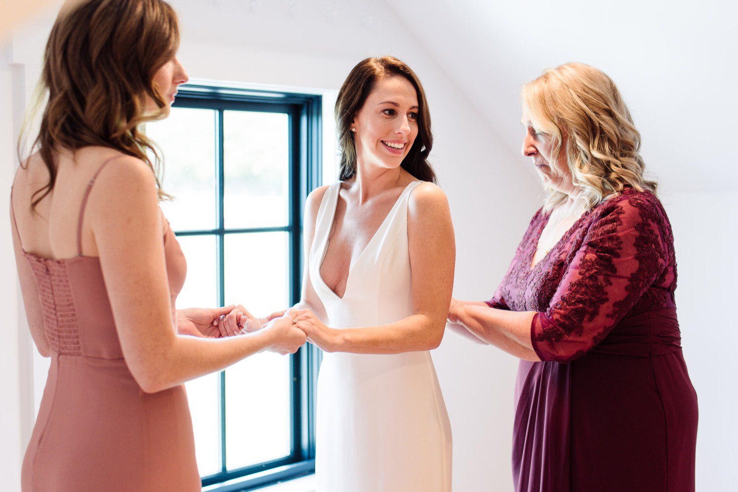 Bride smiling as mother and bridesmaid adjust dress