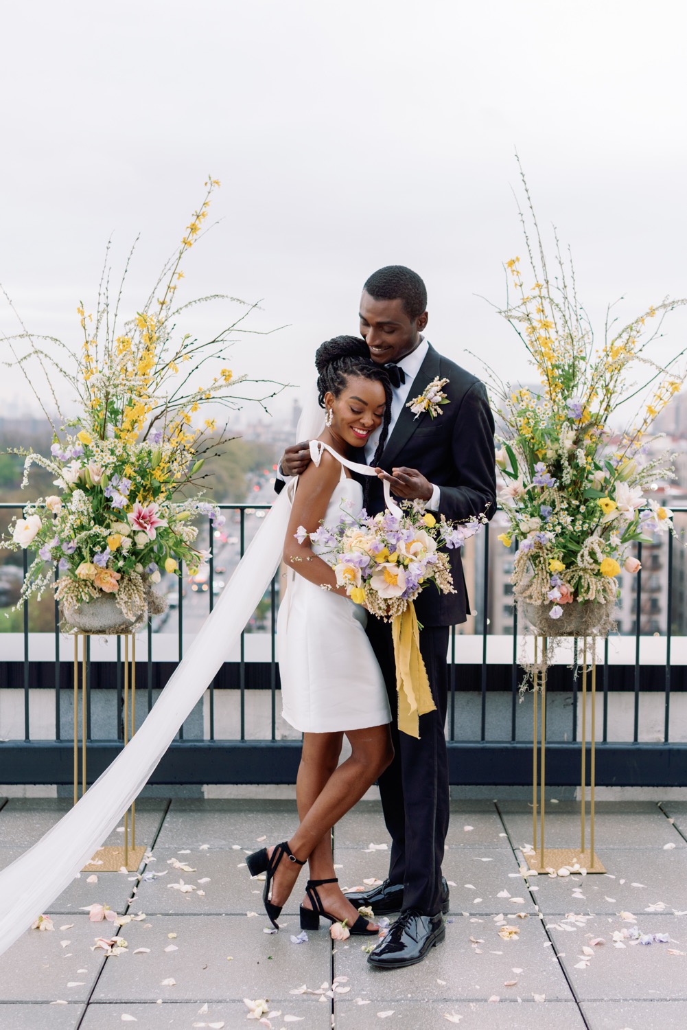 Bride and groom embrace on balcony with bouquet and flower stands over NYC backdrop real wedding alexandra grecco mini dress odette