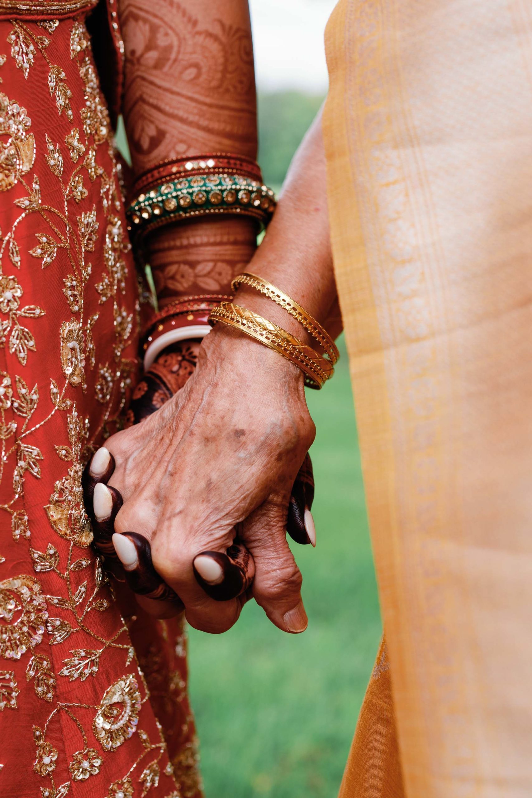 closeup of bride and grandmother holding hands in traditional Indian dress
