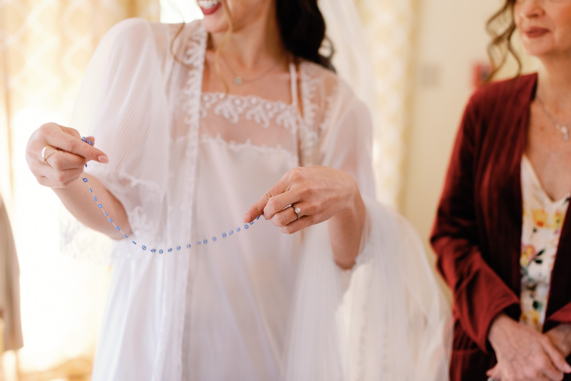 a bride smiles wearing shawl holding blue gemstone necklace