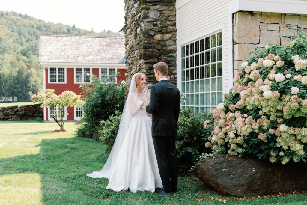 bride and groom at riverside farm vt wedding with flowering bushes on a fall wedding day